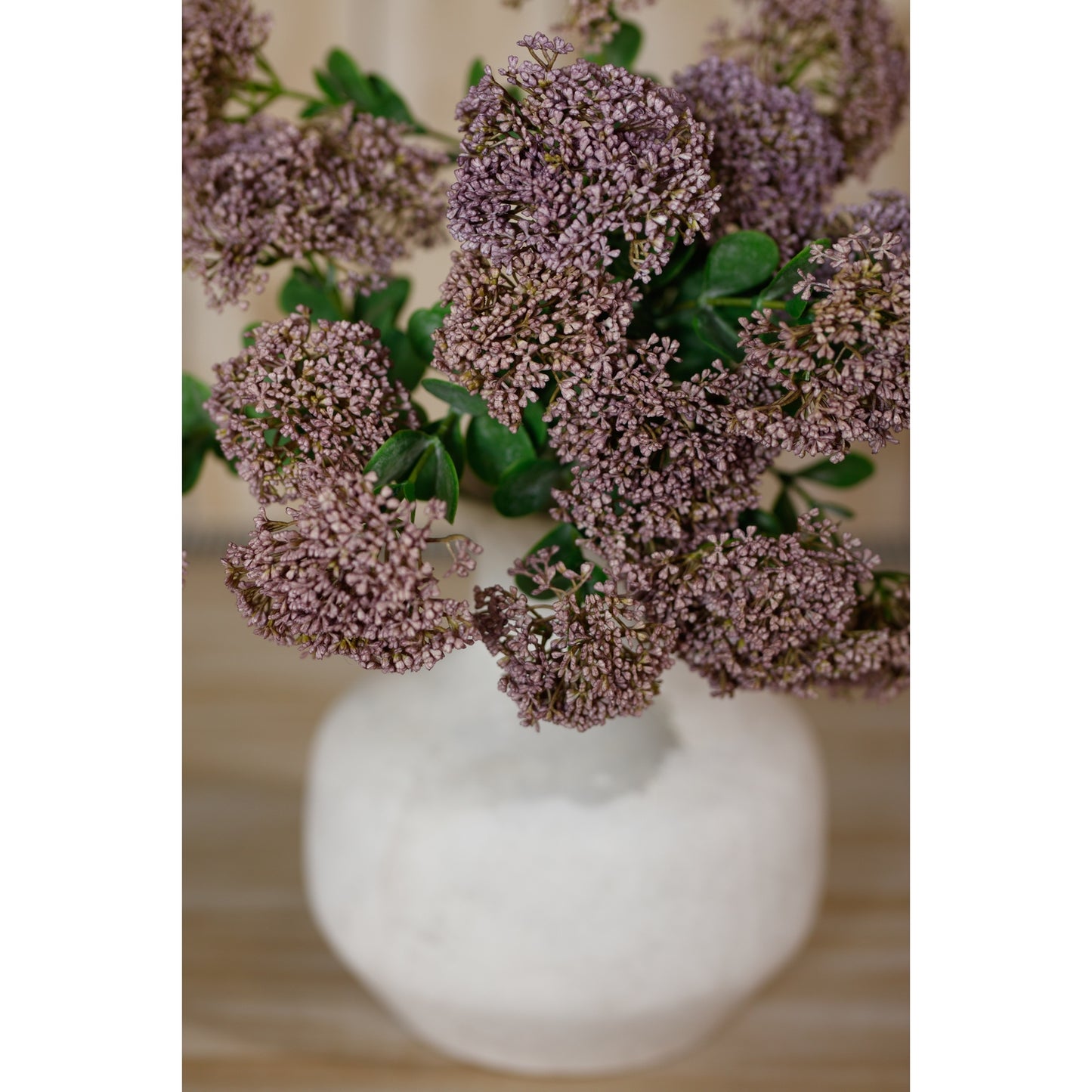 Purple sedum flowers with delicate blooms and lush green leaves, arranged in a white vase, adding elegance to any space.