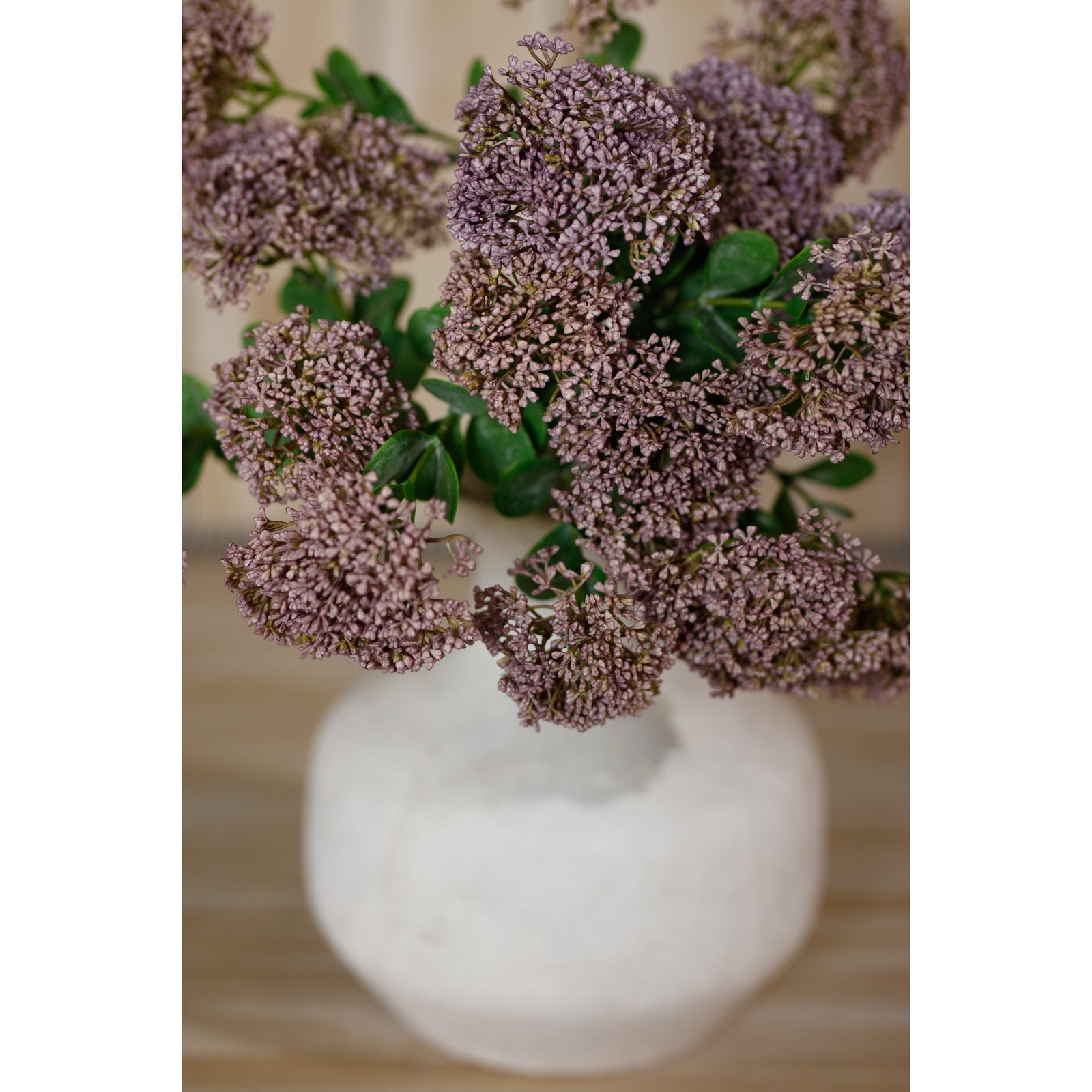 Purple sedum flowers with delicate blooms and lush green leaves, arranged in a white vase, adding elegance to any space.