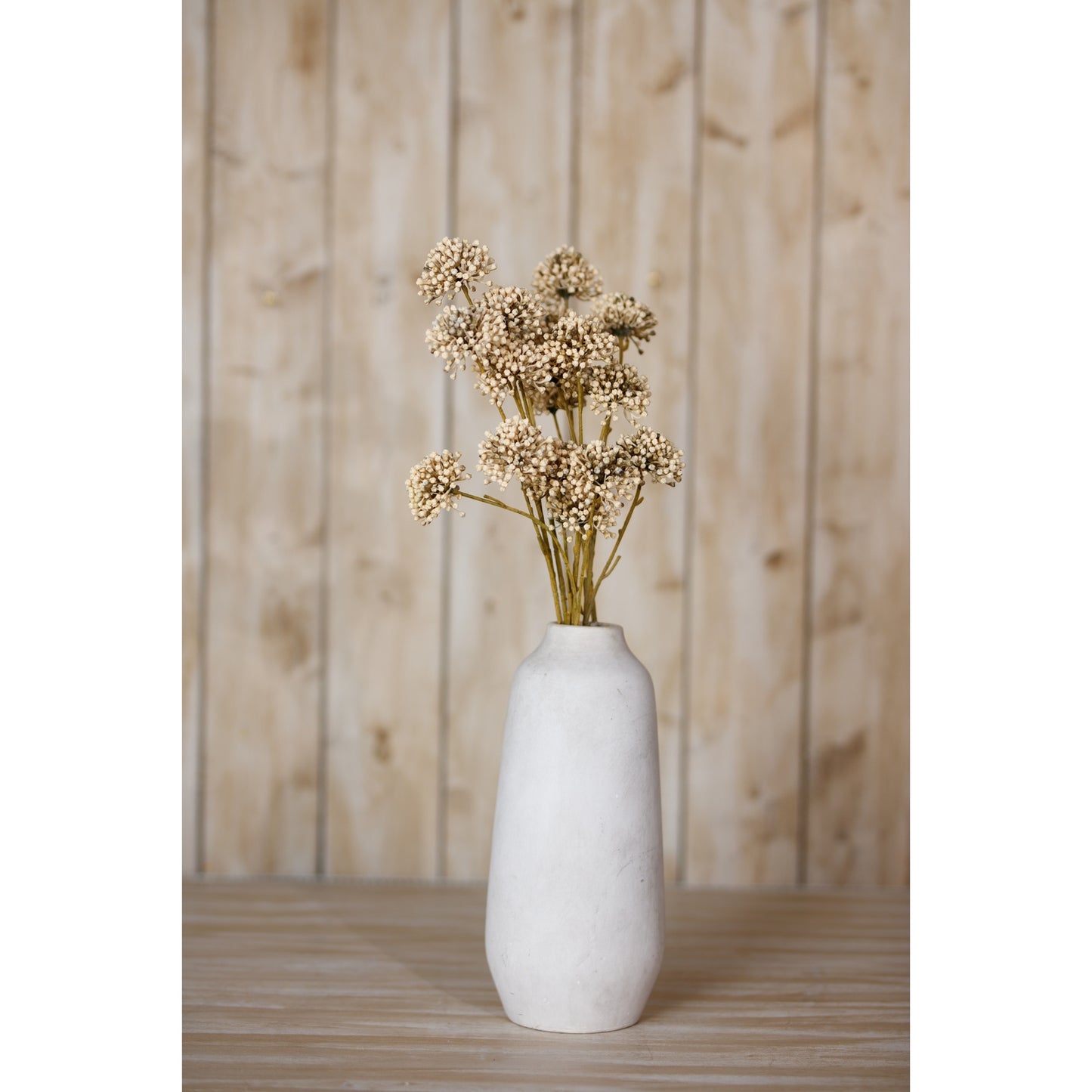 Brown allium spray features spherical, lifelike blooms in earthy tones, arranged elegantly in a minimalist white vase against a wooden backdrop.