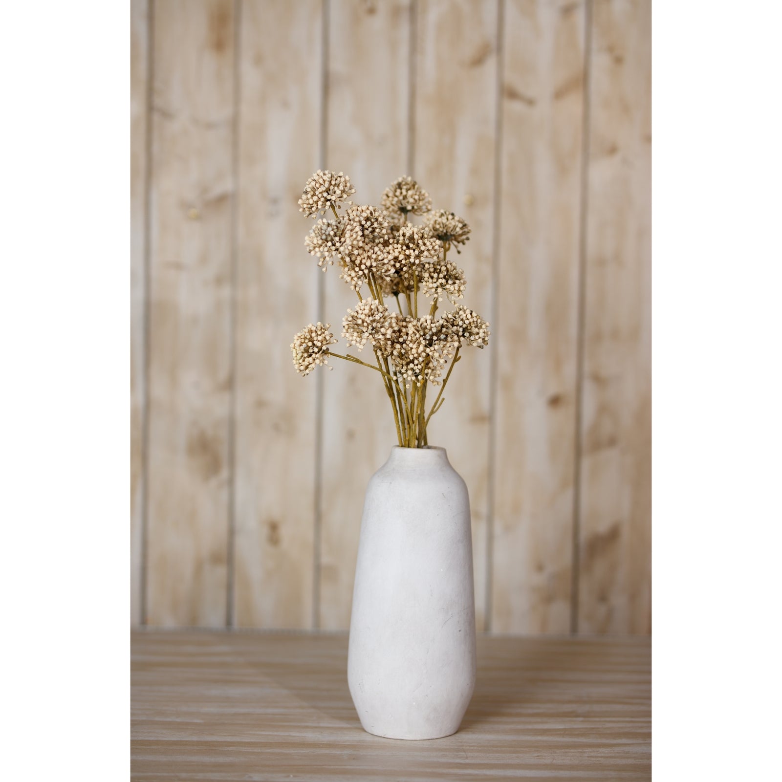 Brown allium spray features spherical, lifelike blooms in earthy tones, arranged elegantly in a minimalist white vase against a wooden backdrop.