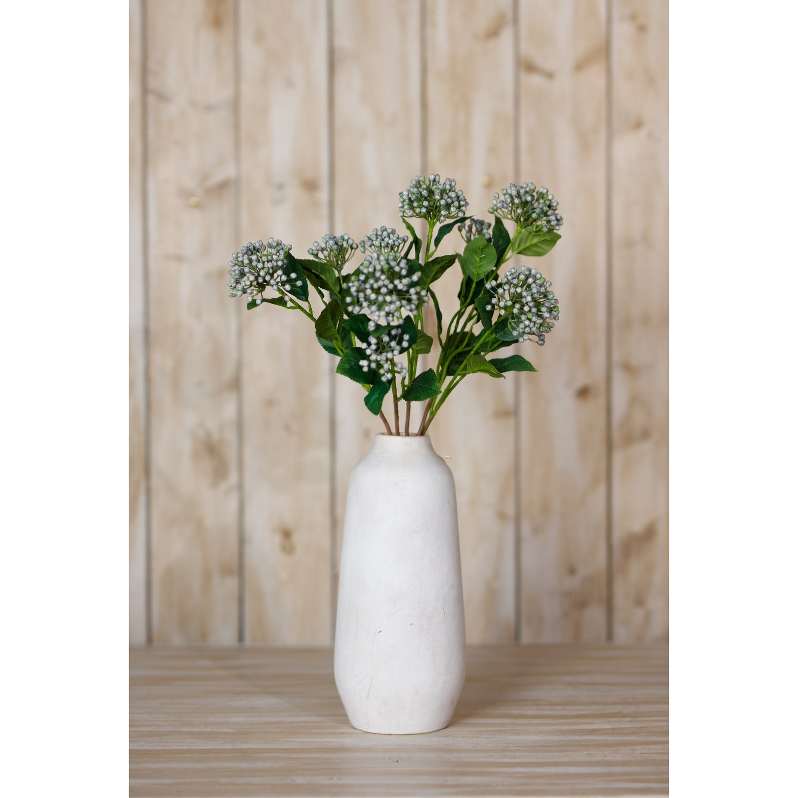 Lifelike blue budding hydrangea spray in a matte white vase, set against a rustic wooden background, adding vibrant elegance to any decor.