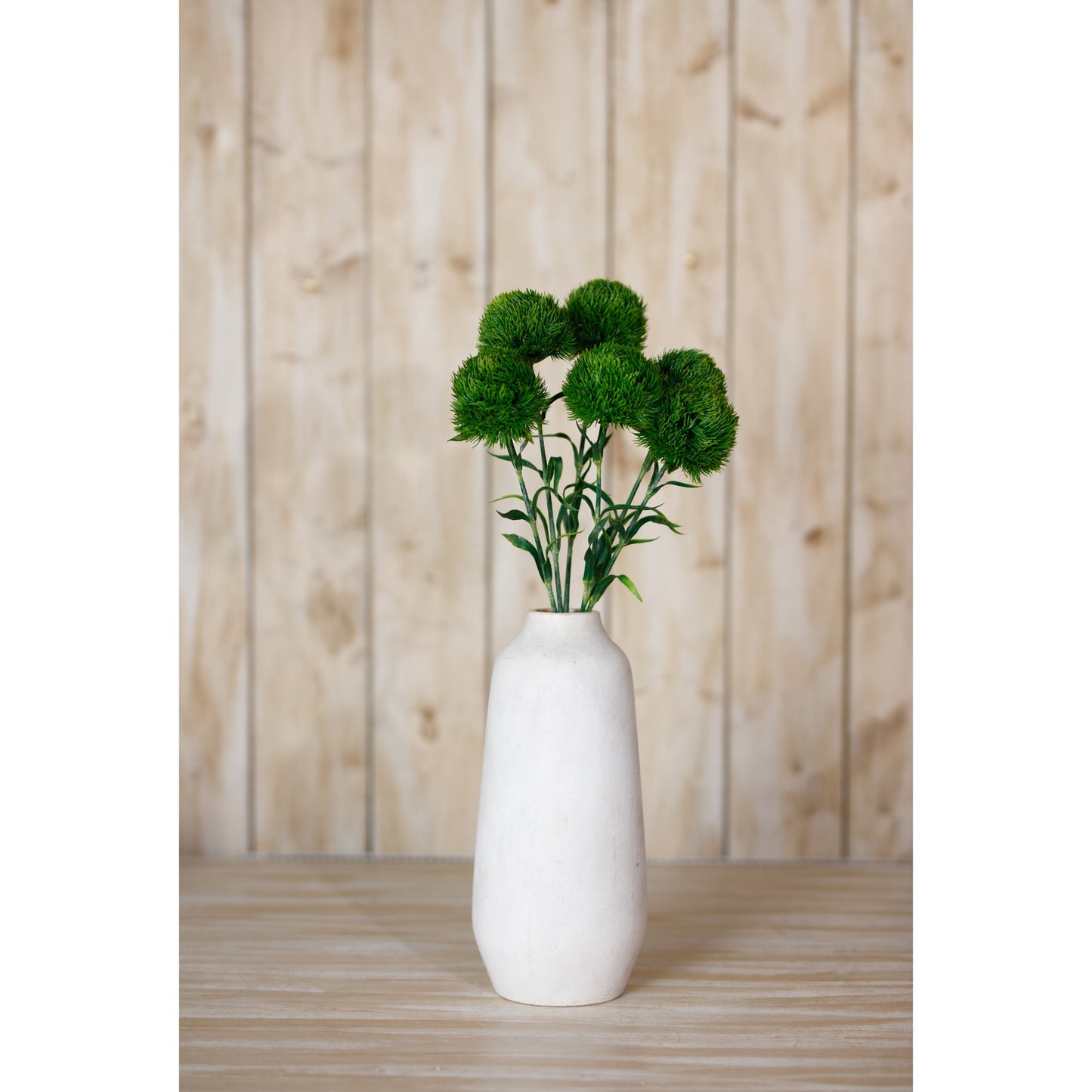 Dark green artificial Dianthus stem in a white vase, set against a wooden backdrop, adding elegant charm to any space.