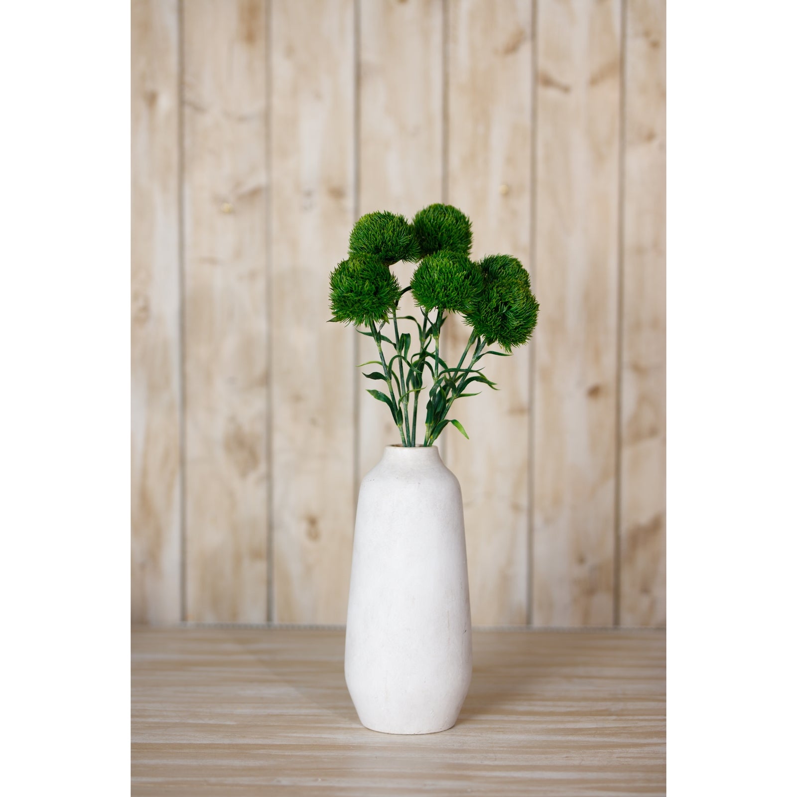 Dark green artificial Dianthus stem in a white vase, set against a wooden backdrop, adding elegant charm to any space.