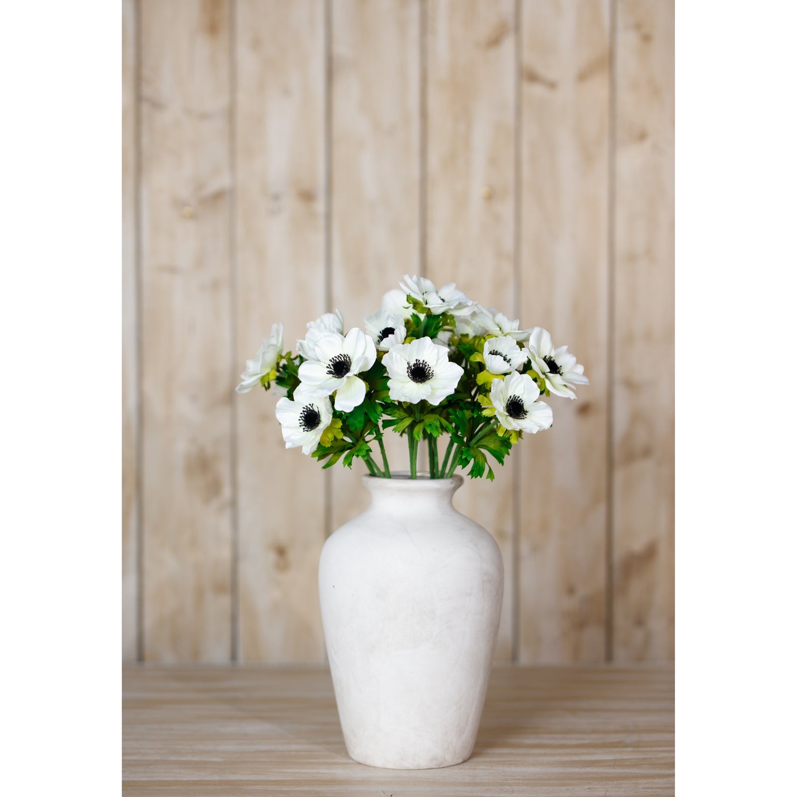 White anemone spray in a smooth, white vase, showcasing delicate petals and dark centers against lush green foliage.