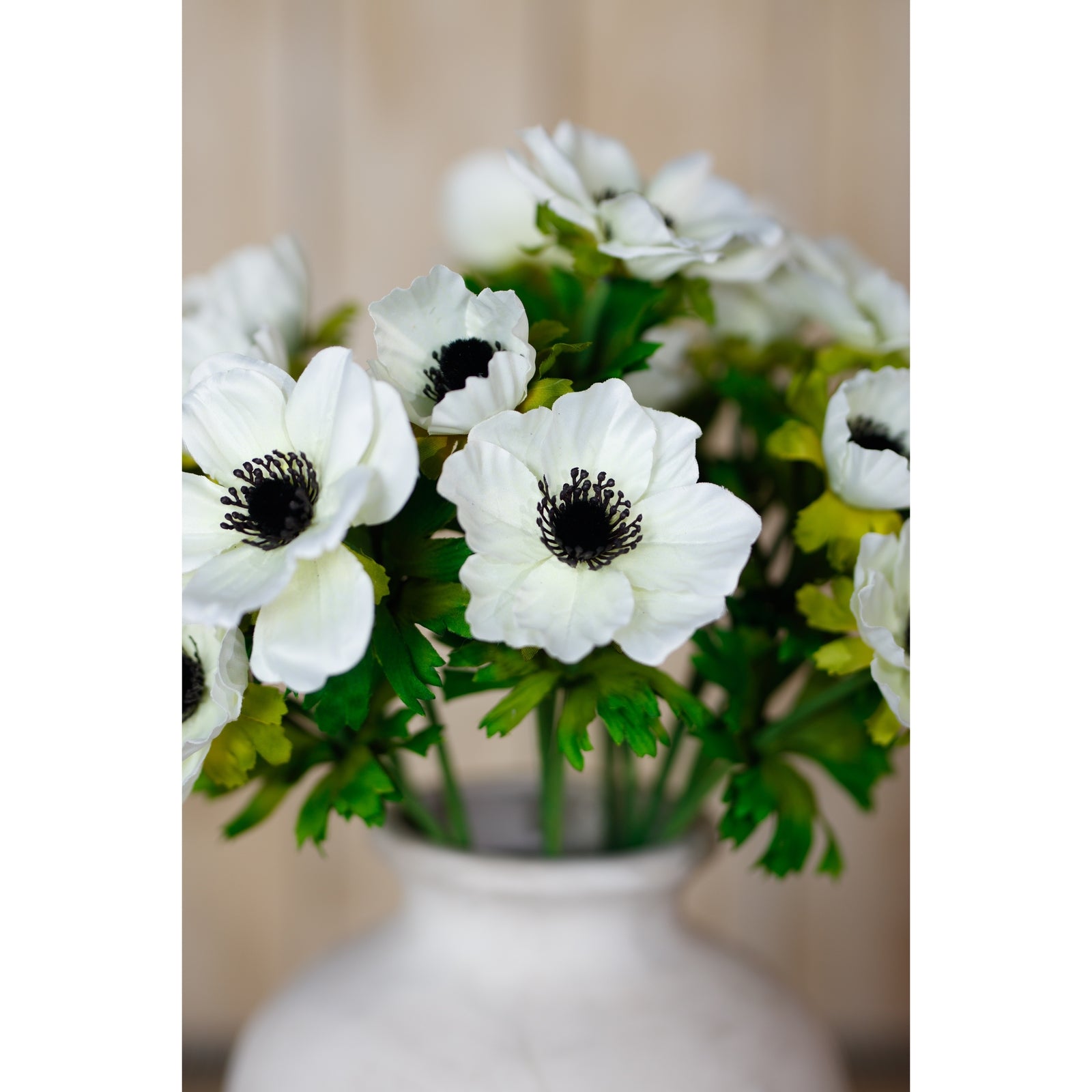 White anemone spray featuring delicate petals with black centers and lush green foliage, elegantly arranged in a vase.