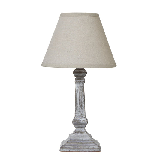Distressed grey column base table lamp topped with a neutral linen shade, creating a warm, inviting ambiance.