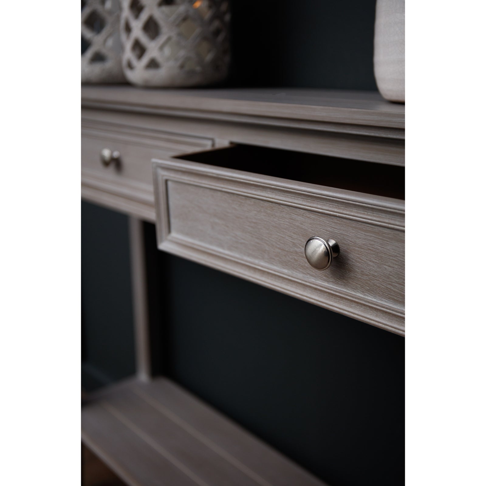 Distressed grey console table featuring four drawers with elegant detailing and sleek metal knobs, set against a dark background.