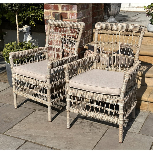 Pair of elegant outdoor dining chairs with light beige HDPE rattan weave and plush, removable cushions, set on a stone patio.