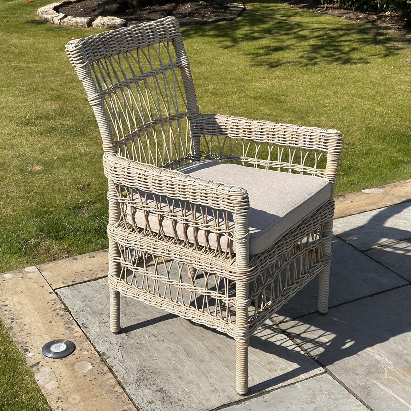 Provence Collection outdoor dining chair with a chunky HDPE wicker weave, light gray cushions, and a rust-resistant frame, set on stone patio.