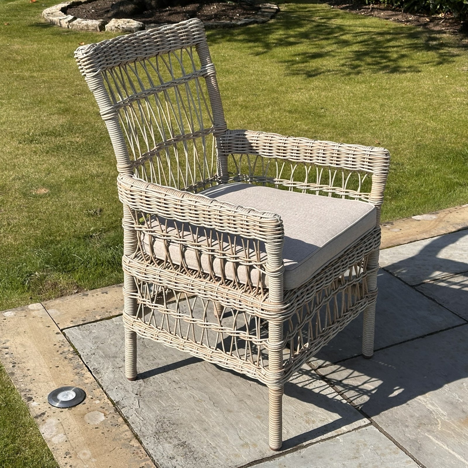 Provence Collection outdoor dining chair with a chunky HDPE wicker weave, light gray cushions, and a rust-resistant frame, set on stone patio.