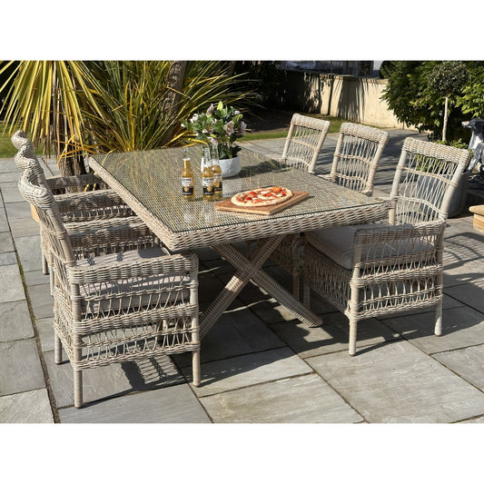 Provence Collection 6-seater outdoor dining set with light wicker chairs, a glass-top table, and cushions, on a stone patio.