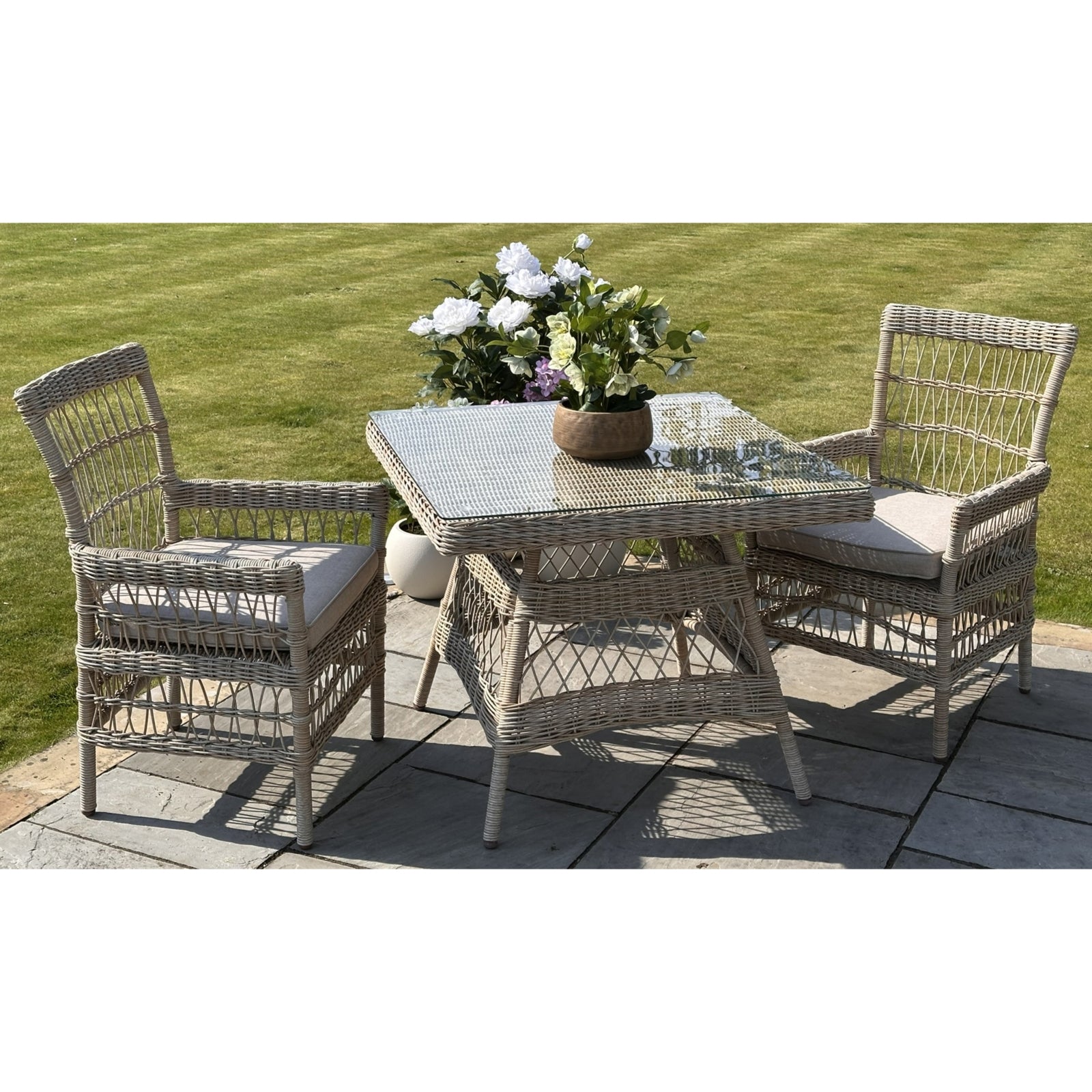 Sophisticated outdoor dining set featuring weatherproof HDPE rattan and cushioned chairs with a square glass table. Elegant, neutral tones.