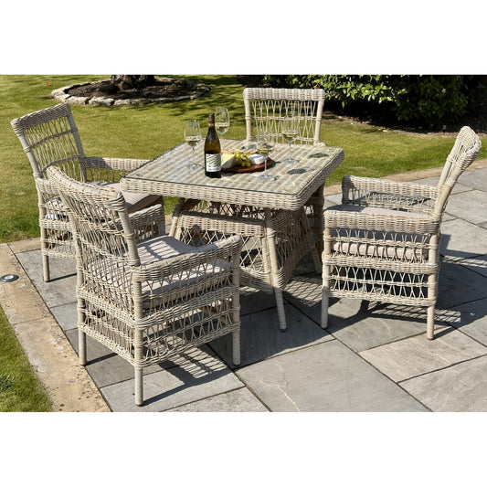 Provence Collection outdoor dining set featuring a square table and four chunky, woven rattan chairs, set on stone patio with wine and glasses.