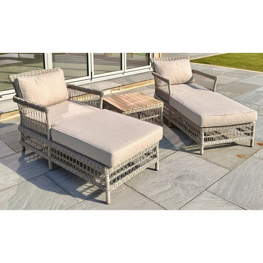 Stylish outdoor sun loungers in grey rattan with plush cream cushions and a matching side table on a stone patio.