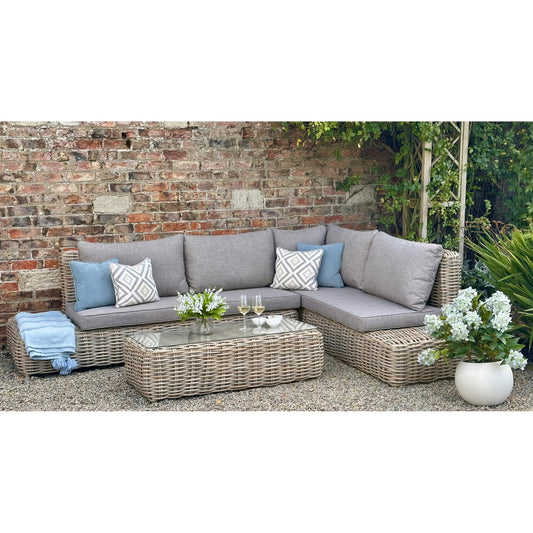 Amalfi Collection large corner outdoor seating set featuring grey cushions, geometric pillows, and a glass-top coffee table, set against a brick wall.