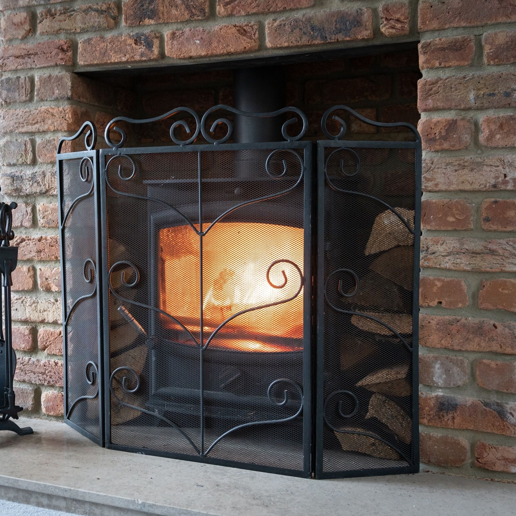 Large black ornate fire screen featuring intricate detailing, robust construction, and a sophisticated design, enhancing fireside elegance.